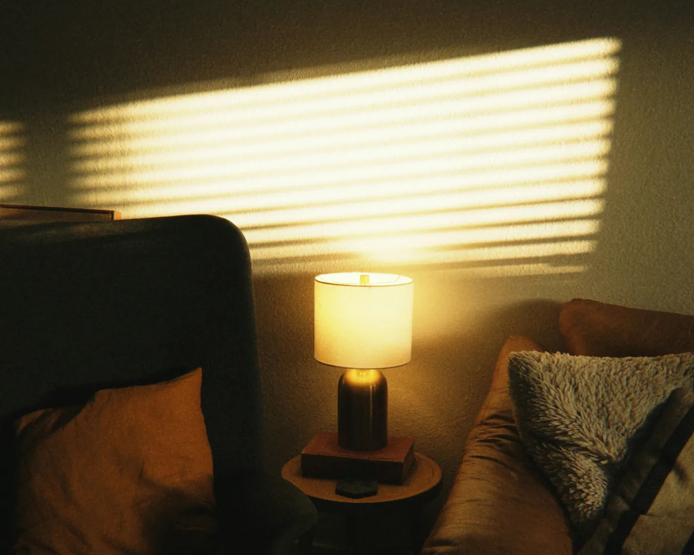 A lit table lamp between two armchairs with soft light stripes on the wall in the evening