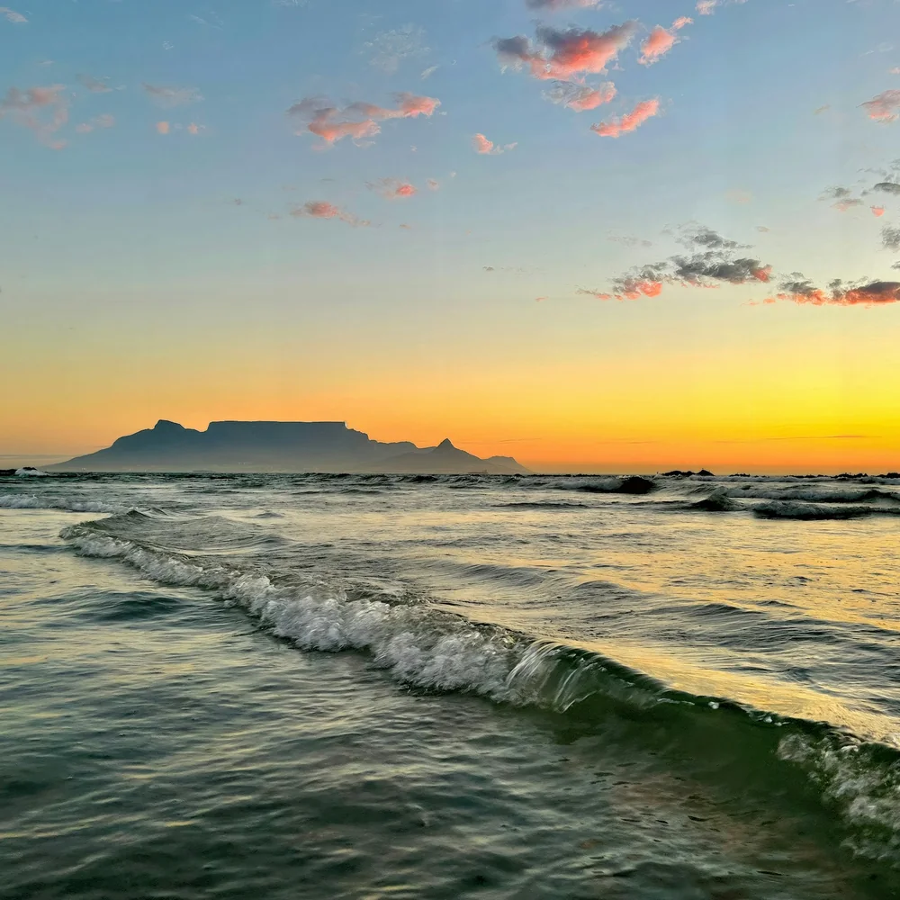 Table Mountain in silhouette across a bright sea at sunset, waves catching the light