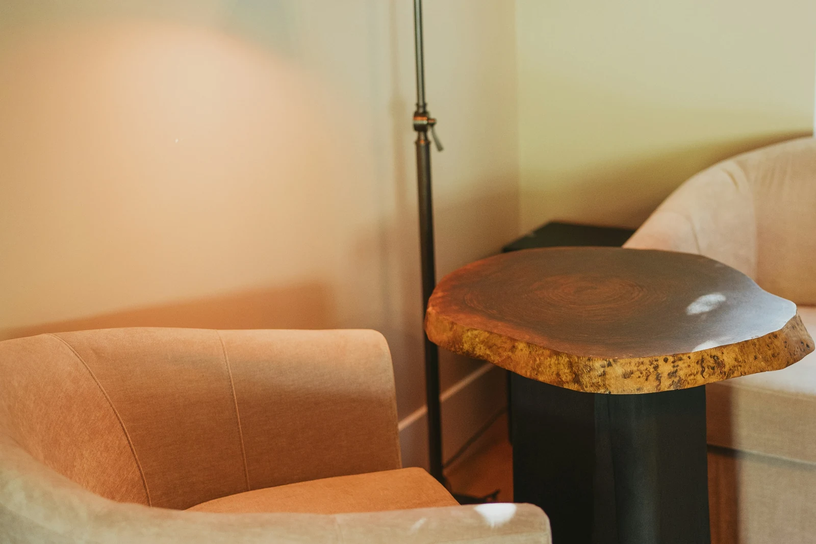 Two empty armchairs facing a live-edge wood side table under a warm reading lamp, in a quiet corner of a room