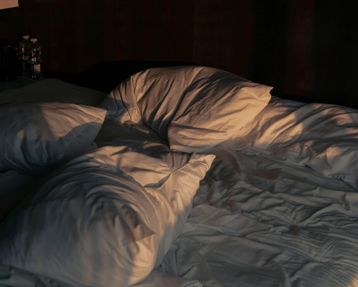 Morning sun on rumpled pillows and a white duvet on an unmade bed