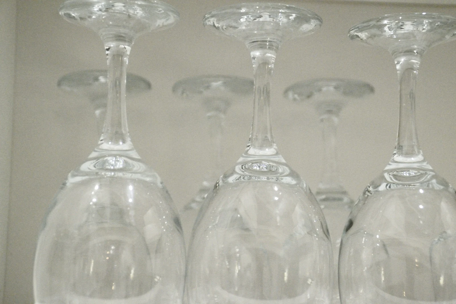 Wine glasses standing upside down on a light grey shelf, empty and clean