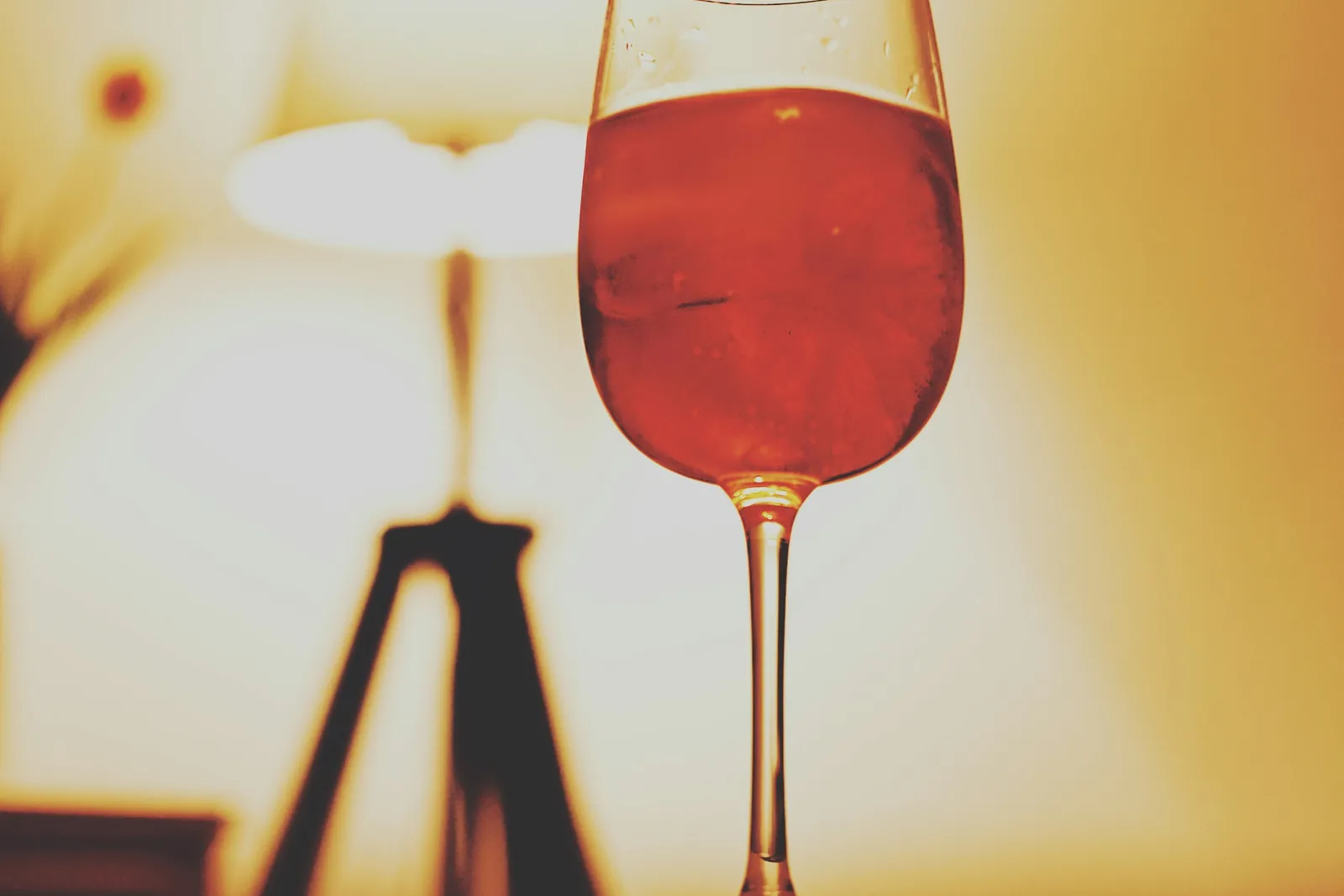 A half-full glass of red wine in warm evening light beside a blurred table lamp