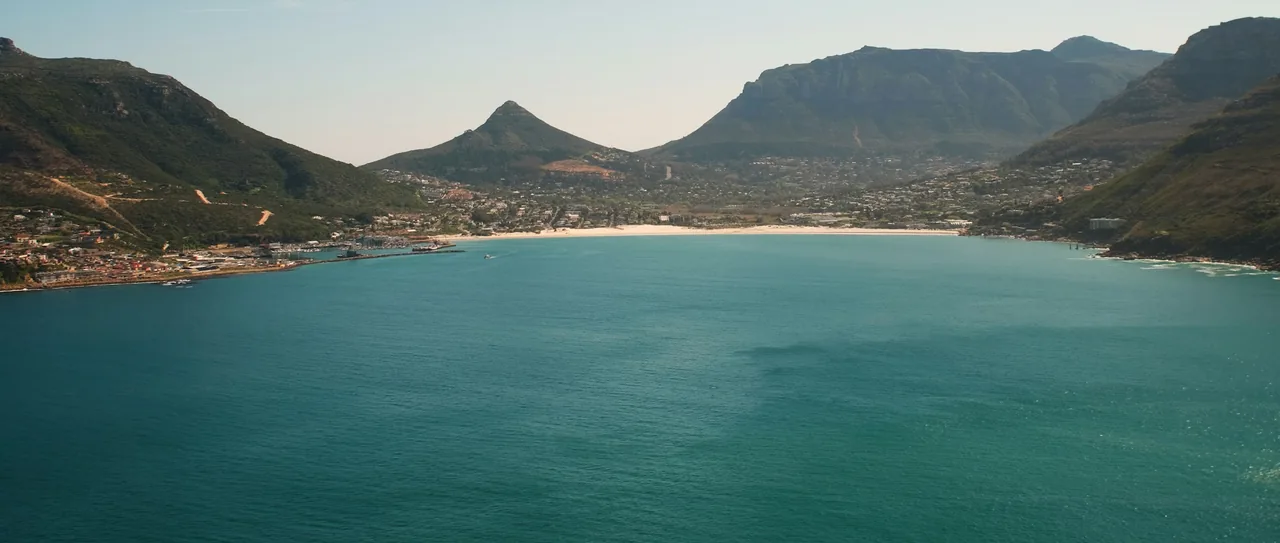 Turquoise water of Hout Bay below green mountains and a white beach, Cape Town
