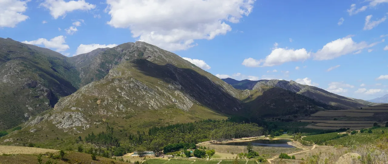 A green mountain valley with farmland below a blue sky with scattered clouds