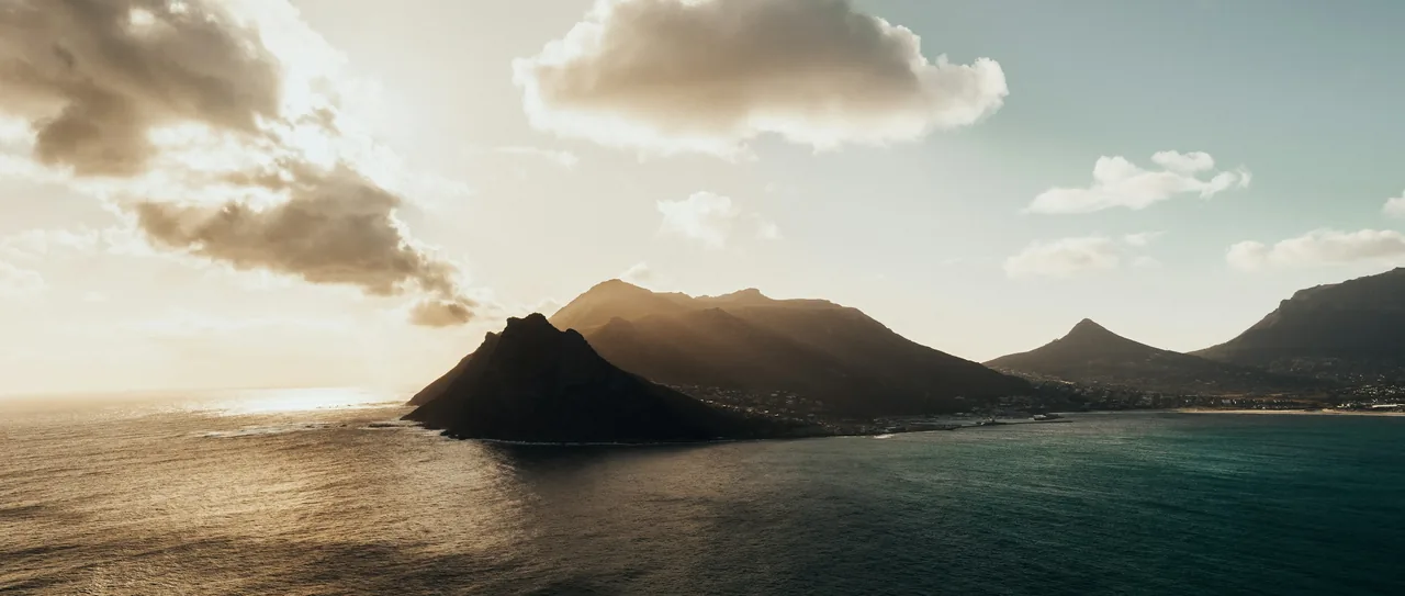 Hout Bay mountains in hazy golden light above dark water, Cape Peninsula