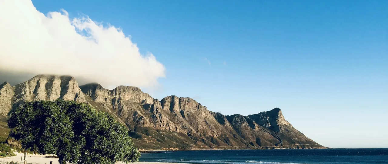 A sandy beach below a rocky mountain ridge under a clear blue sky