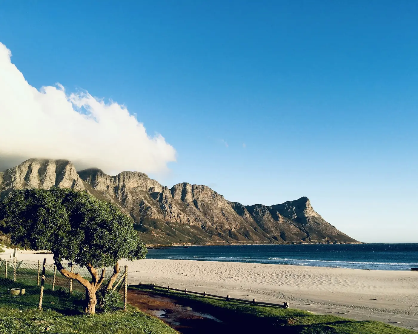 A sandy beach below a rocky mountain ridge under a clear blue sky
