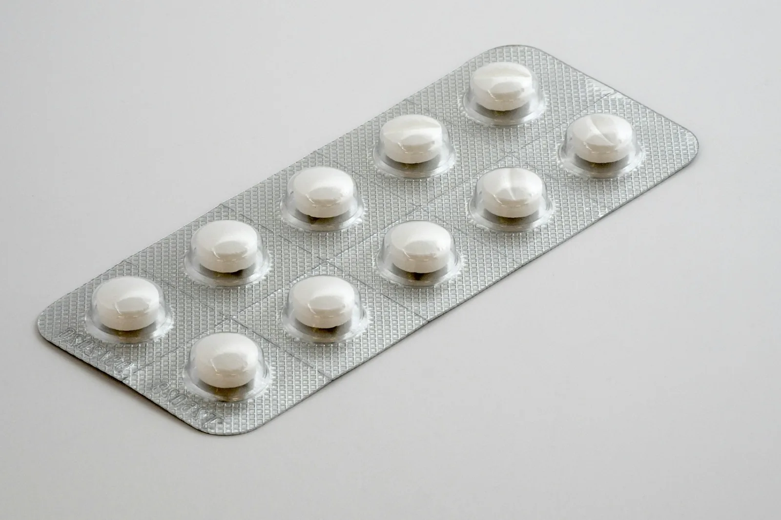 A silver blister pack of ten white round tablets on a pale grey surface
