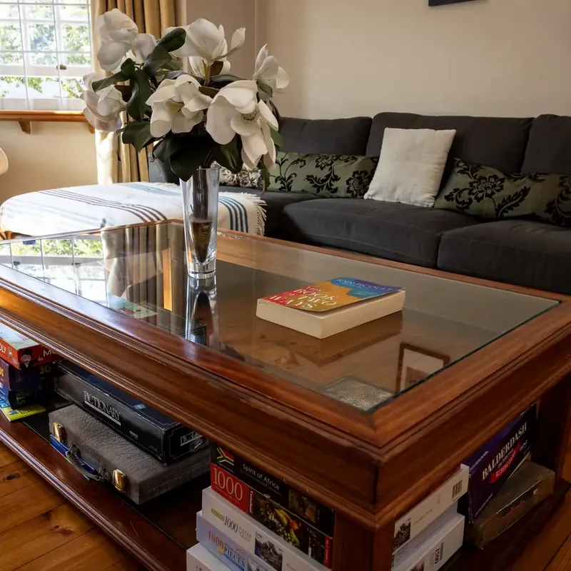 A sunlit lounge with a wooden coffee table, a paperback and white magnolia flowers in a glass vase