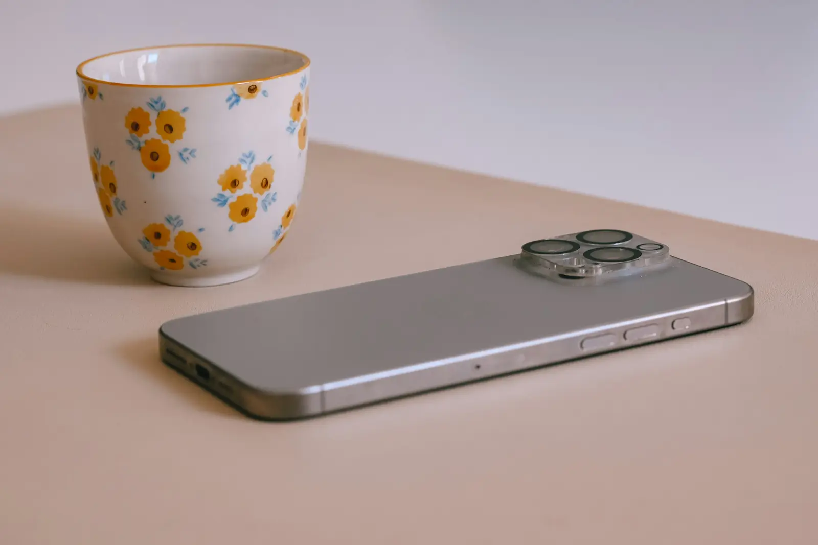 A floral cup and a smartphone lying on a table in soft daylight