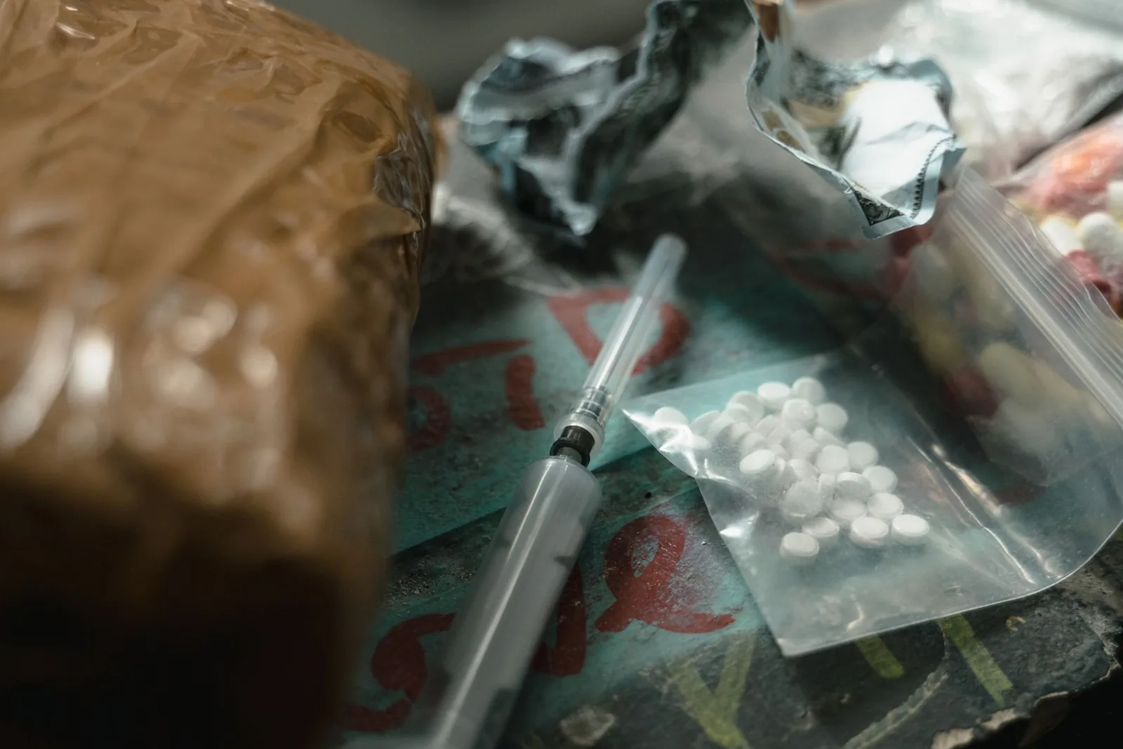 A brown block of heroin wrapped in plastic beside crumpled foil, a syringe and a bag of pills