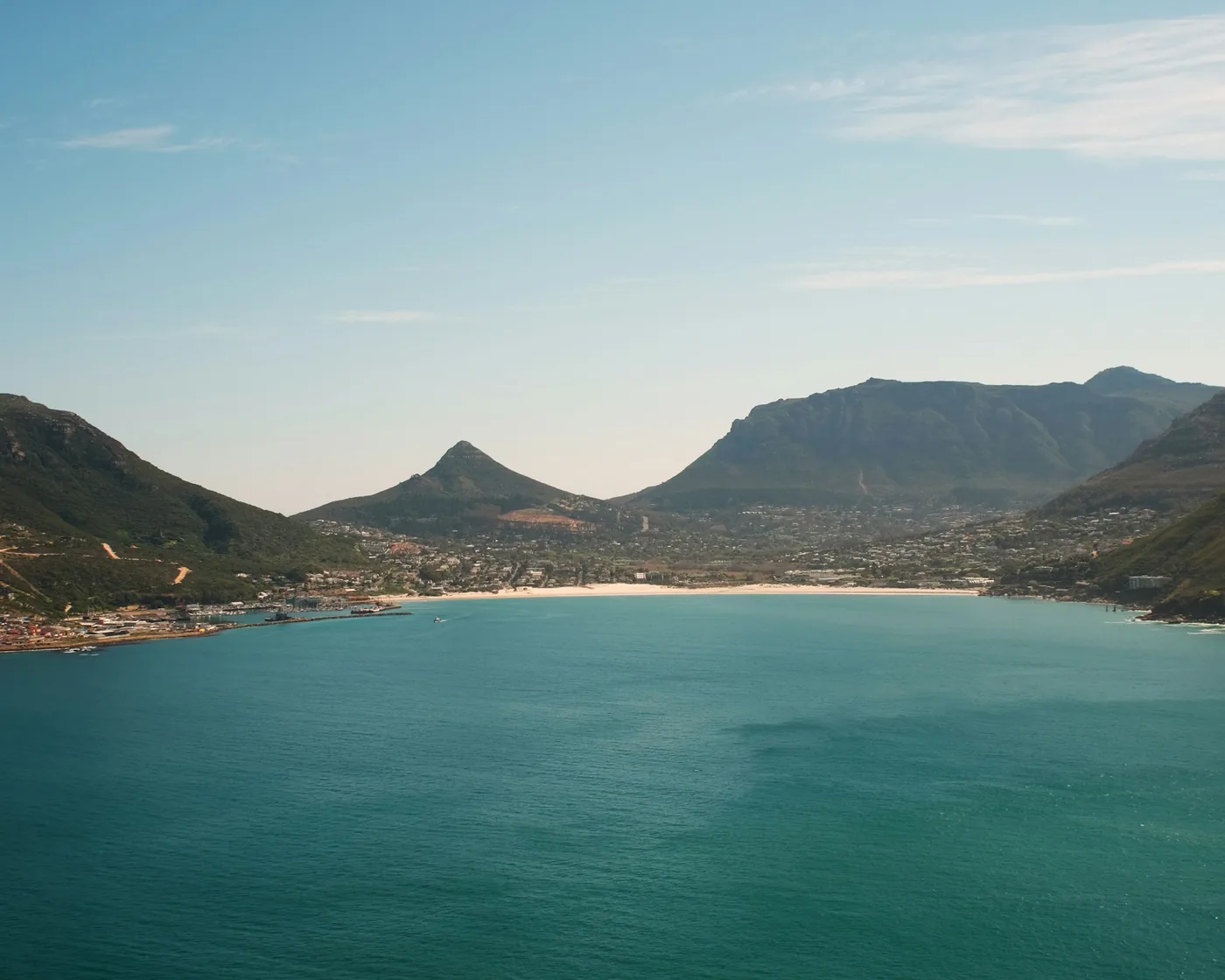 Turquoise water of Hout Bay below green mountains and a white beach, Cape Town