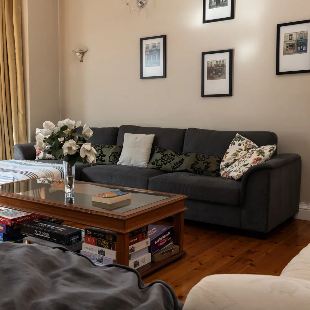 A sunlit lounge at the centre with a grey sofa, cushions and white magnolia flowers in a glass vase