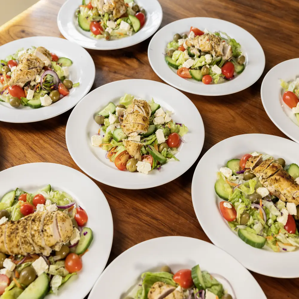 Plates of chicken salad on a wooden table at the centre, seen from above