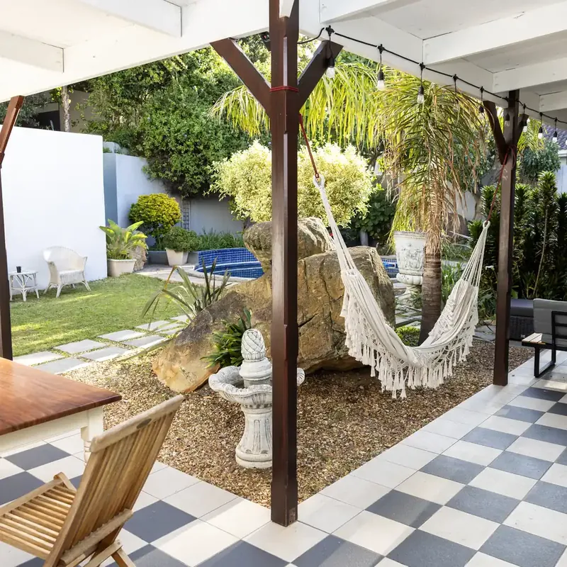 A covered patio at the centre with a white hammock, wooden chairs and a black and white tiled floor