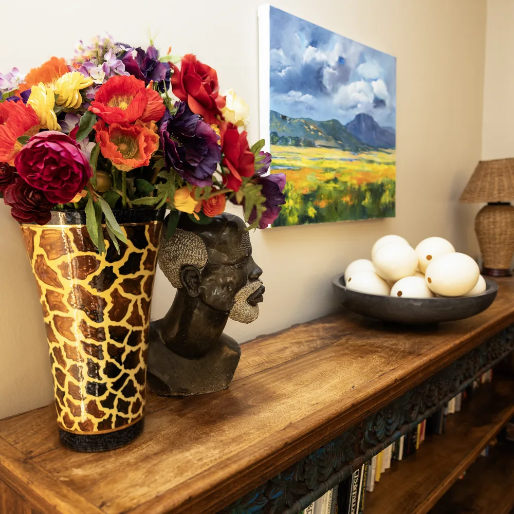 A vase of bright flowers beside a painting and a bowl on a wooden sideboard