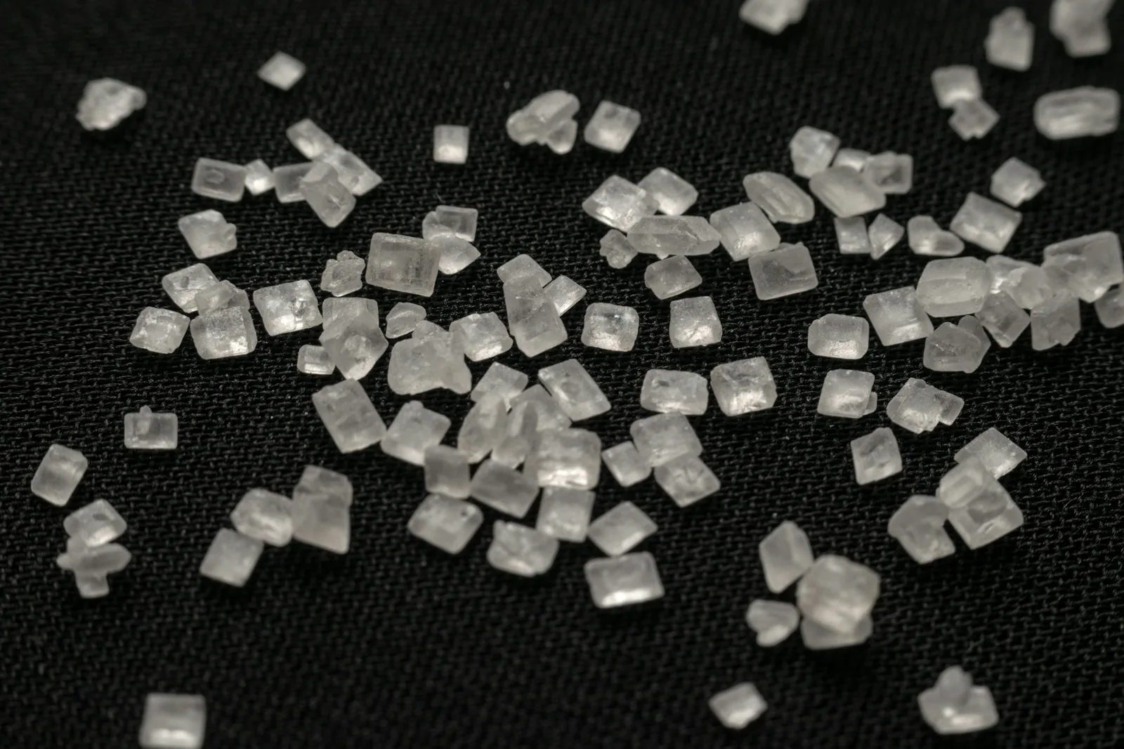 Small clear sugar crystals scattered on a dark fabric