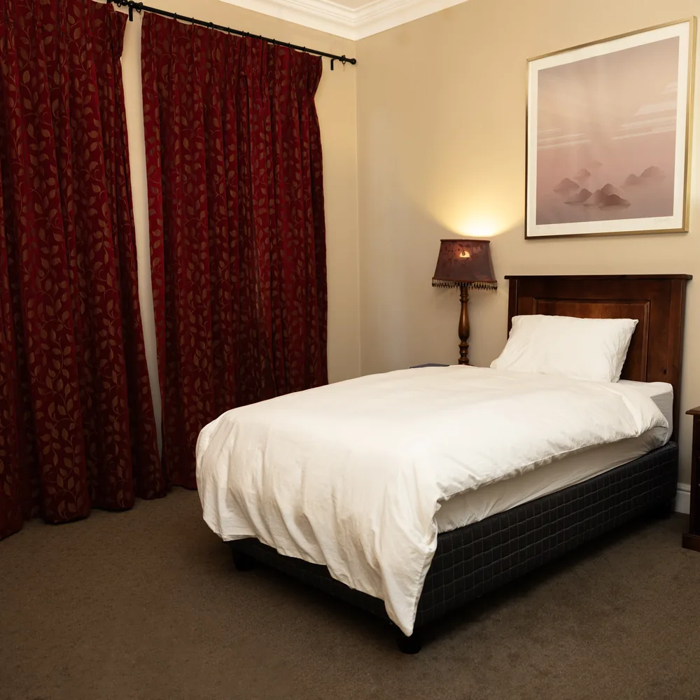 A single bedroom with white linen and bedside lamps at our rehab in Lakeside, Cape Town