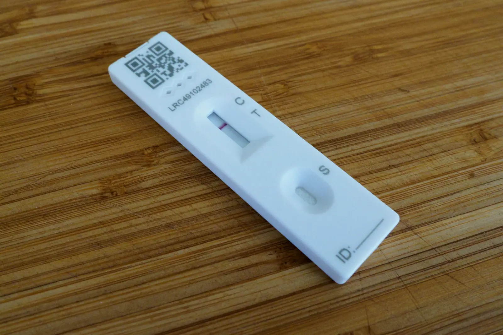 A white rapid test cassette on a wooden board, its result window marked C and T with a line at C