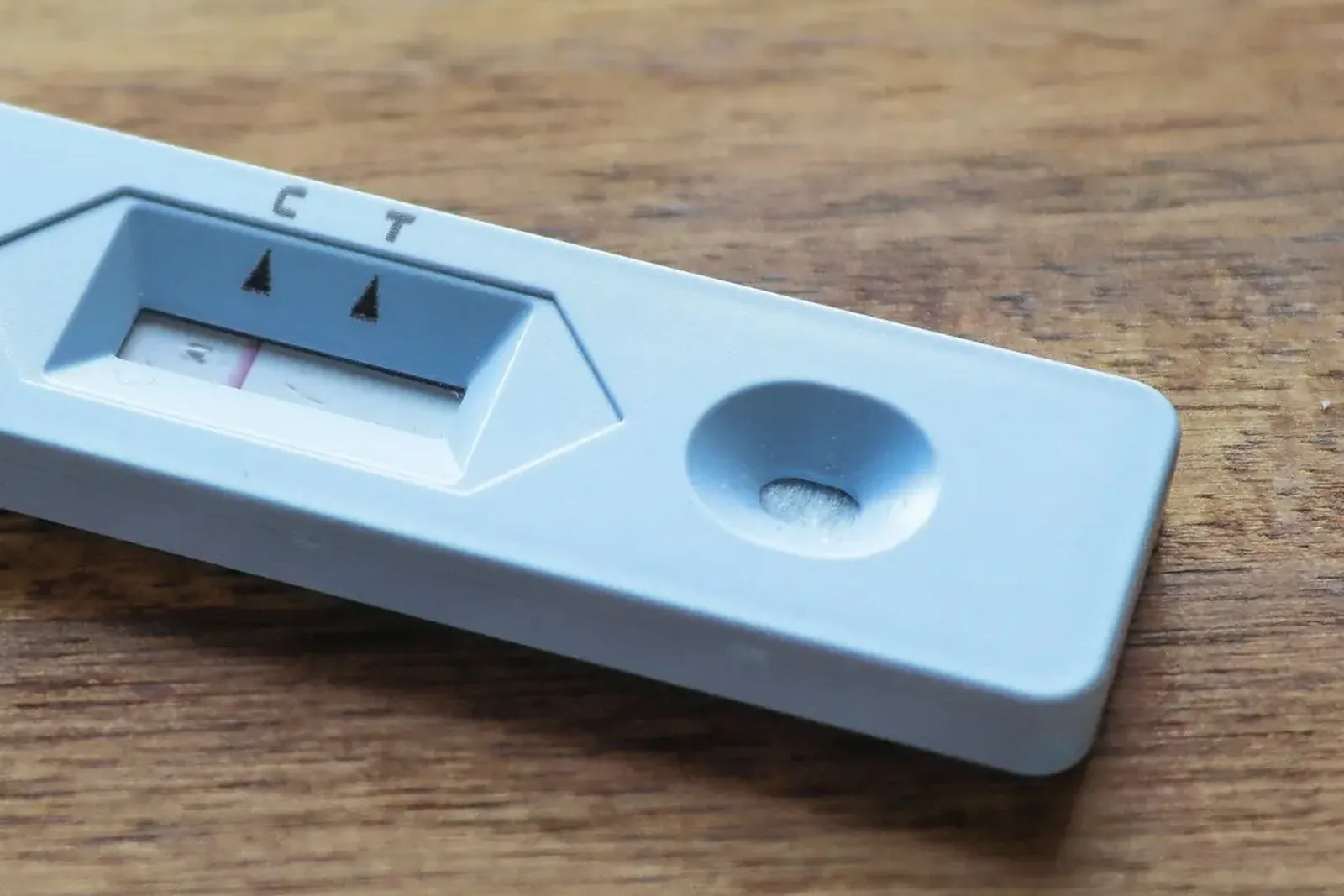 A single-use rapid test cassette on a wooden table, its result window marked C and T