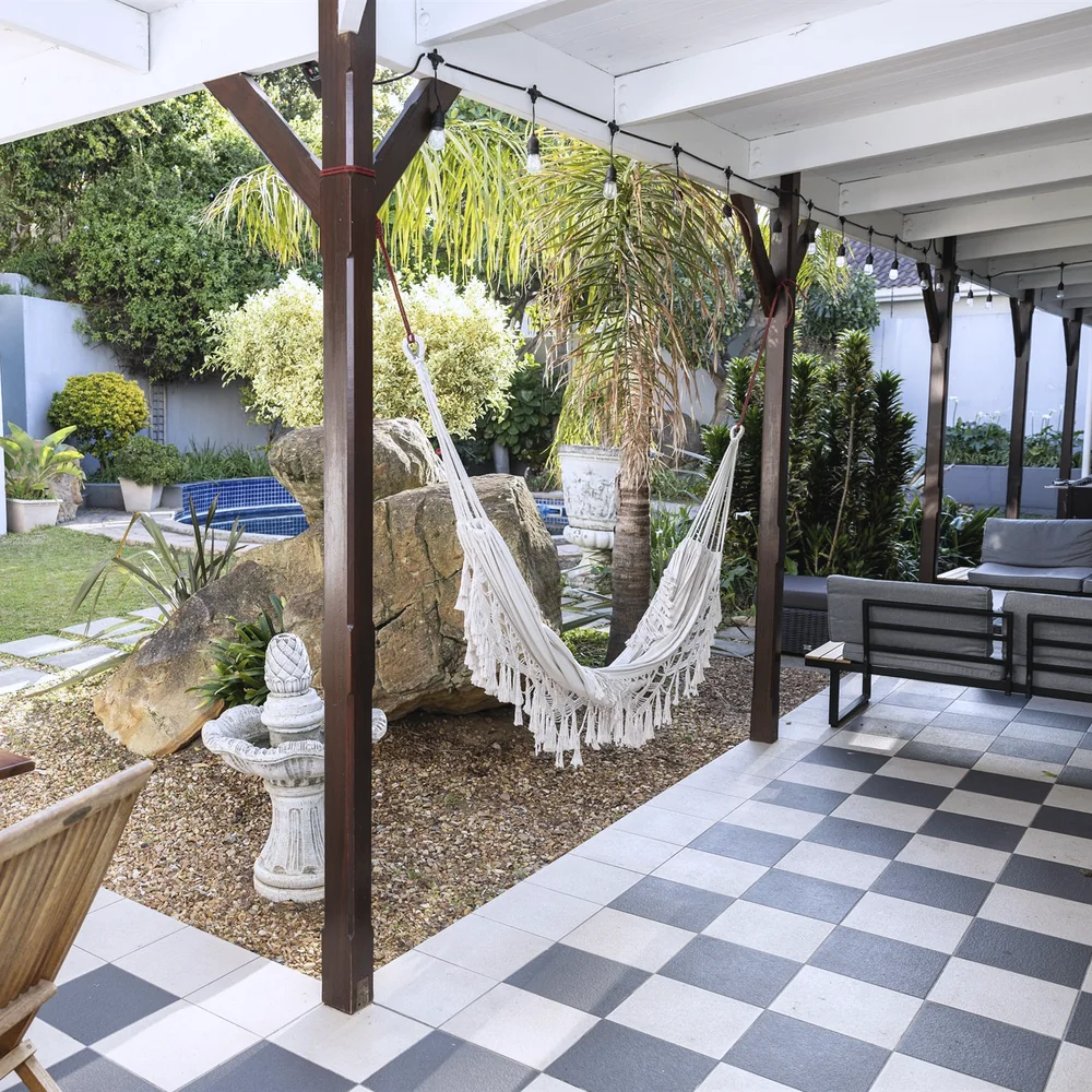 A garden veranda with a woven hammock, palm tree and pool corner under a checkerboard-tiled roof