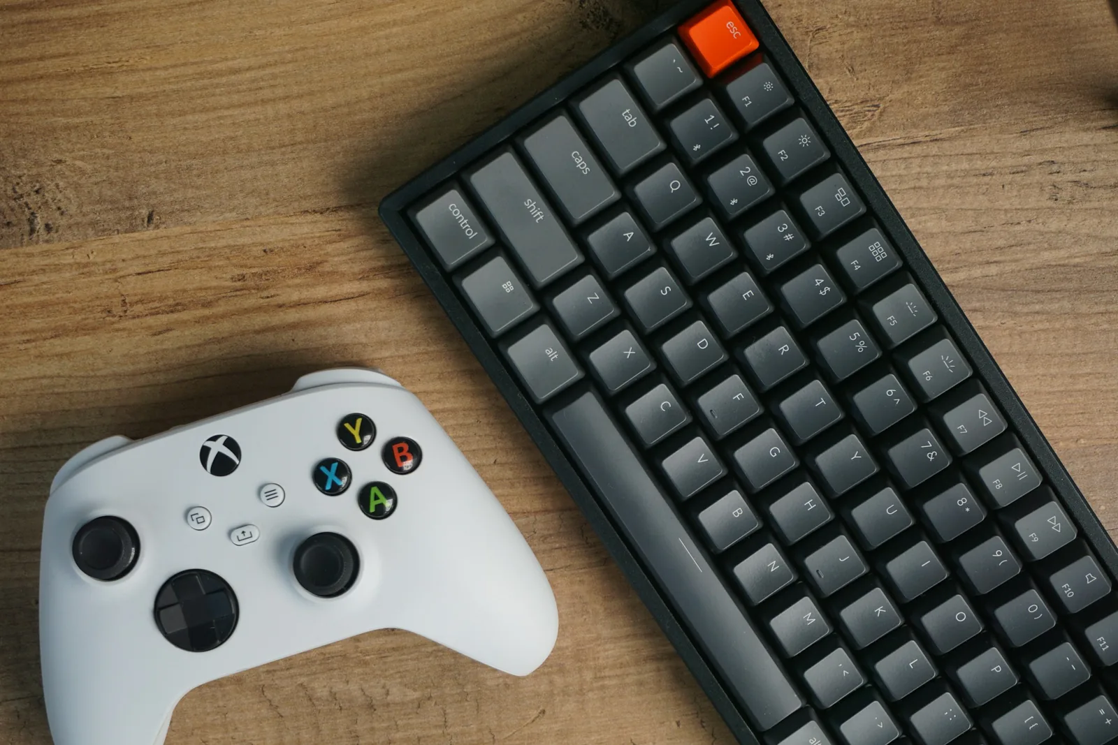 White game controller next to a compact mechanical keyboard on a light wooden desk