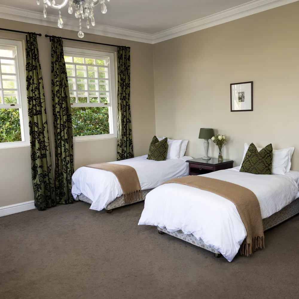 A bright bedroom with two made beds and green curtains at Renewed Life Center