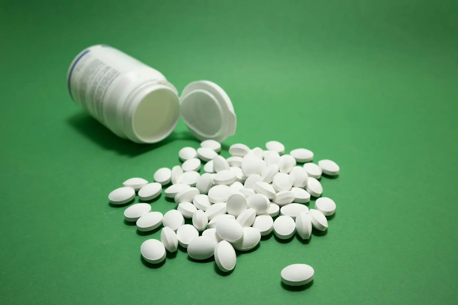 White oval tablets spilled from an open white bottle onto a green surface