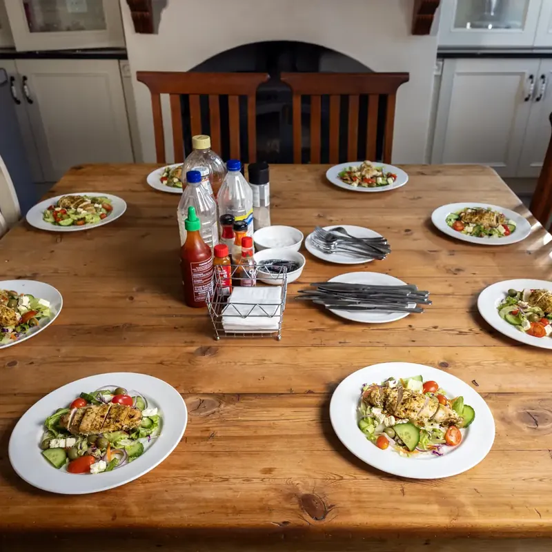 A long wooden dining table set with plates of chicken salad in a bright room at the centre